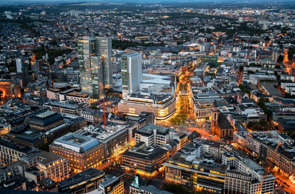 View of Frankfurt from a skyscraper at sunset, Germany. Multiple office and residential buildings, central square, illumination SSUCv3H4sIAAAAAAAACnRSwW7DIAy9T9o/RJwbLSlZS3bcYaftC6oeHOI2qAQqIJ2mqv8+CKHlsN3w8/Oz/cz1+akoSAdWcPJWXEPkYyHlZJ0BJ7TycLVacIOqR5MjF0M3VQ5gL5w2AmQOduD4oGBED6pJygDf5iSxDtxk0YbuC8TB4dFrRPAuEUfcxbhIiTnpK3yKvE9C9kId7csnqH4Ec7JkldHs1AXal/ZLqCKxSWLE9v9qW6HQ2pcPoUBx/FNYWI5SgkI92YdsfOyTGXBExX8eq4UeBr3XFwwjo8u39Mn6rrSPj1lw8cqgRIj27WIHcvp2aMbcUJh6oTMvL5qDDASaKZ2N4MGNR5l2w3zsVMb1pJwJk5O0PZFan6GT4bAHr4kJH8BaT+8TnjXi/mvpMeujtJsXWFRJ7+8fwprSirWUbrYt2zbbirKFEP/MILzOPE4S8jE/iT5fXYQJSL1hzZa16/JAsS0bzqoSXrt1WXXAmpoy5M3Bu3z7BQAA//8DAAwrrvoOAwAA